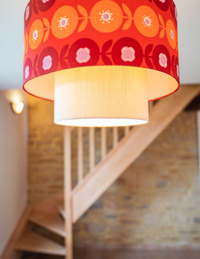 Retro red and orange chandelier with large pink flowers in the living room of this Airbnb holiday home. In the background, a wall of exposed local stone and a rough wooden staircase.