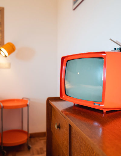 vieille télévision rétro orange des années 70 déposée sur un meuble seventies. Le tout dans une chambre 2 personnes d'une maison de vacances située dan les ardennes belges à Assesse