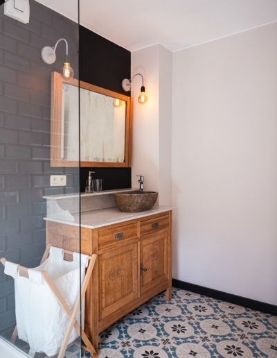 Salle de douche avec vieux carrelages en mosaïque. Meuble avec évier en bois brut et vasque en pierre bleue pour cette maison de vacances au style rétro